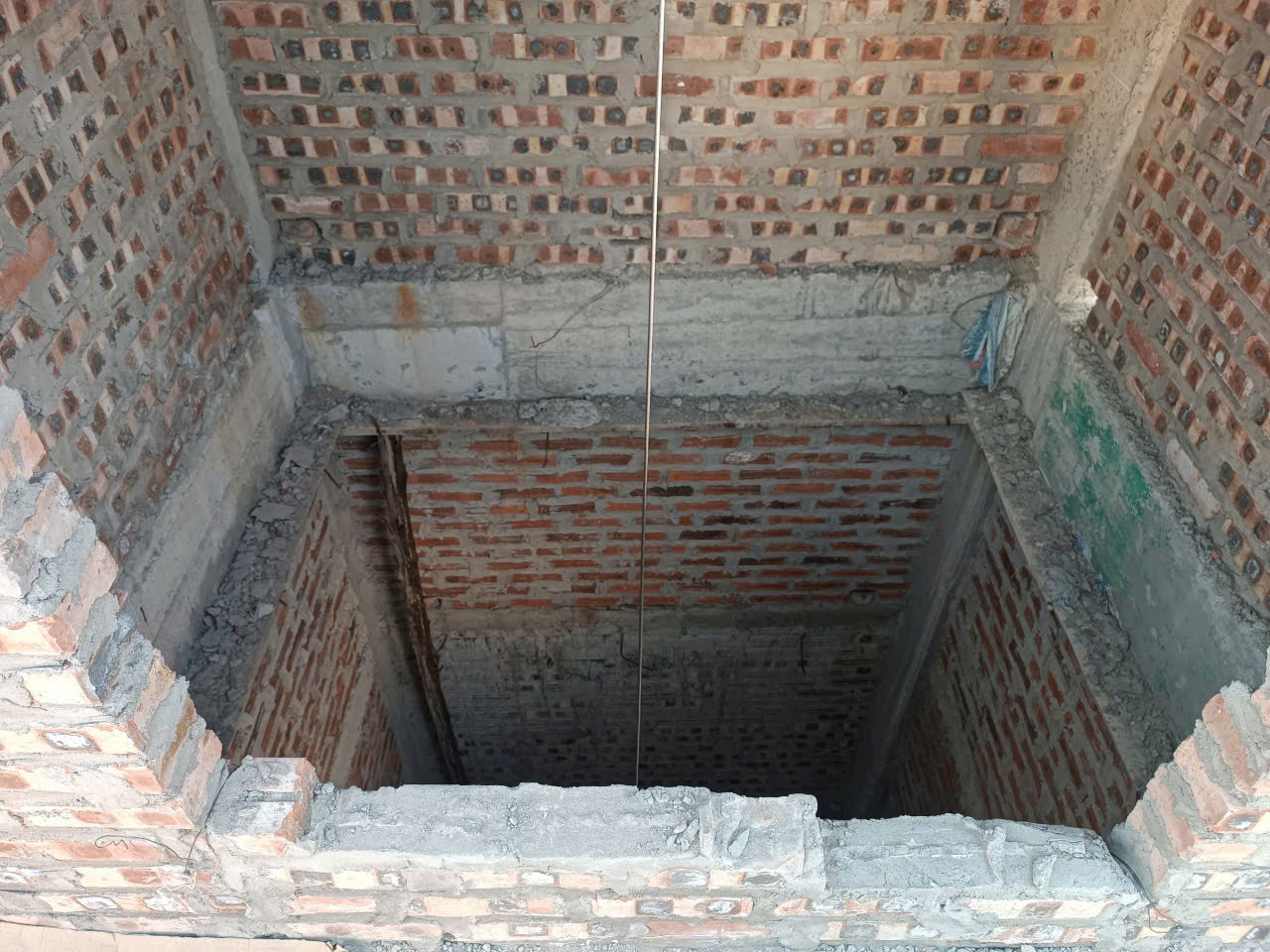 Hố thang máy xây gạch đang thi công trong nhà, tường bê tông gạch đỏ chưa hoàn thiện